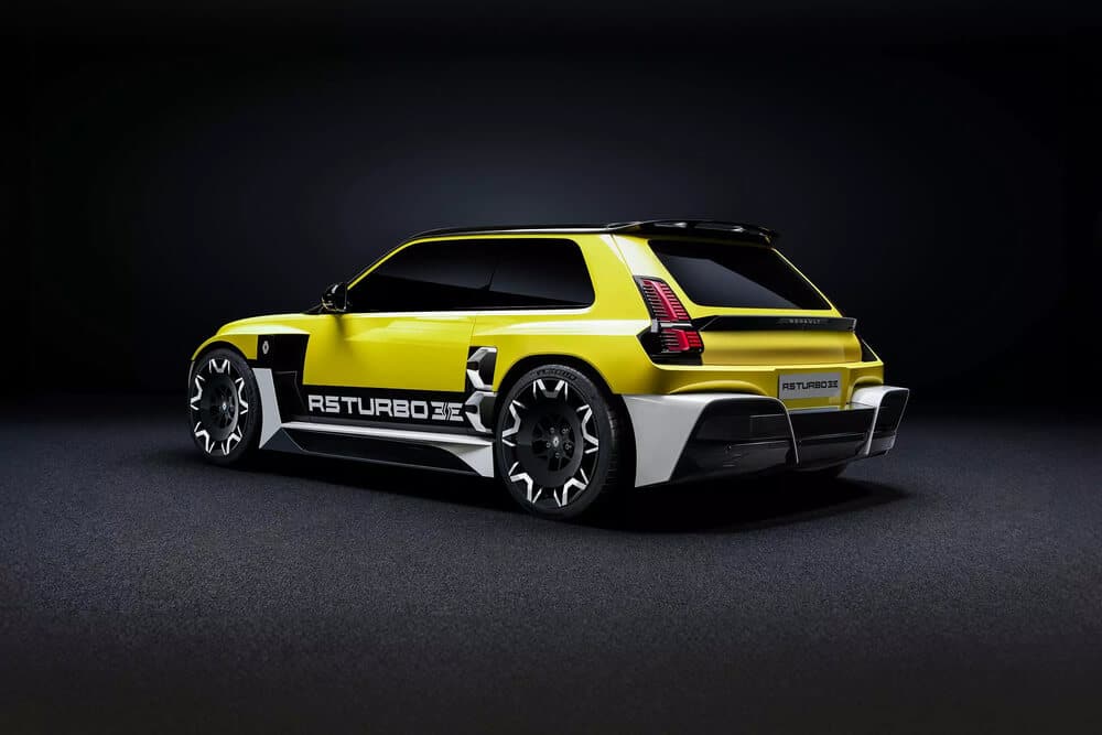 La imagen muestra un coche deportivo moderno con un diseño distintivo. El coche es predominantemente amarillo con detalles en negro y blanco. En el lateral del coche se puede leer el texto 'R5 TURBO 3E'. El coche cuenta con grandes ruedas intrincadas, una carrocería elegante con líneas afiladas y un prominente alerón trasero. Las luces traseras tienen una forma única y el coche tiene una apariencia futurista. Esta imagen es interesante porque muestra un vehículo de alto rendimiento, probablemente diseñado para entusiastas o como una muestra de avances en diseño y tecnología automotriz.