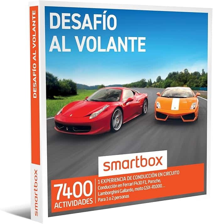 La imagen muestra una caja de producto para "Desafío al Volante" de Smartbox. La caja presenta dos coches deportivos, un Ferrari rojo y un Lamborghini naranja, conduciendo en una pista de carreras. El texto en la caja indica que ofrece 7400 actividades, incluyendo una experiencia de conducción en varios vehículos de alto rendimiento como el Ferrari F430 F1, Porsche, Lamborghini Gallardo y una motocicleta GSX-R1000. La experiencia es para 1 o 2 personas.