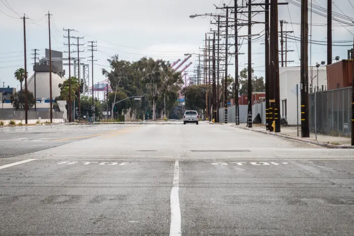 La imagen muestra una escena en Terminal Island, un lugar destacado en la primera película de "Fast and Furious". La carretera vacía y amplia, flanqueada por postes de servicios públicos y líneas eléctricas, es el escenario de la icónica carrera entre el Toyota Supra y el Dodge Charger. Los edificios industriales y las estructuras a ambos lados de la carretera añaden un ambiente auténtico y crudo, característico de las escenas de carreras clandestinas en la película. Esta imagen es interesante y relevante debido a su asociación con una de las carreras más memorables de la franquicia.