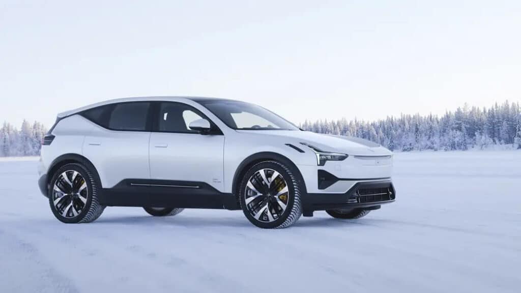 "Un Polestar 3 SUV eléctrico blanco estacionado en un paisaje nevado con un bosque al fondo. El vehículo tiene un diseño elegante y moderno con acentos negros y ruedas grandes y estilizadas. El entorno resalta la capacidad del coche para manejar condiciones invernales, lo que lo hace relevante para mostrar su rendimiento en climas fríos.