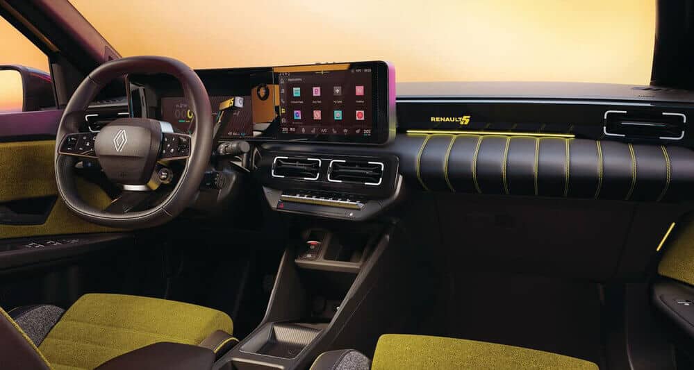 La imagen muestra el interior de un Renault 5 E-Tech. El diseño del tablero es moderno, con una pantalla digital en el centro que parece ser un sistema de infoentretenimiento mostrando varias aplicaciones. El volante tiene múltiples controles y el logotipo de Renault se muestra prominentemente en el centro. Los asientos y el interior tienen un esquema de colores verde y negro con costuras amarillas. El tablero también tiene la marca "Renault 5" iluminada en amarillo. El diseño general es elegante y contemporáneo, destacando la tecnología avanzada y la estética estilizada del coche.