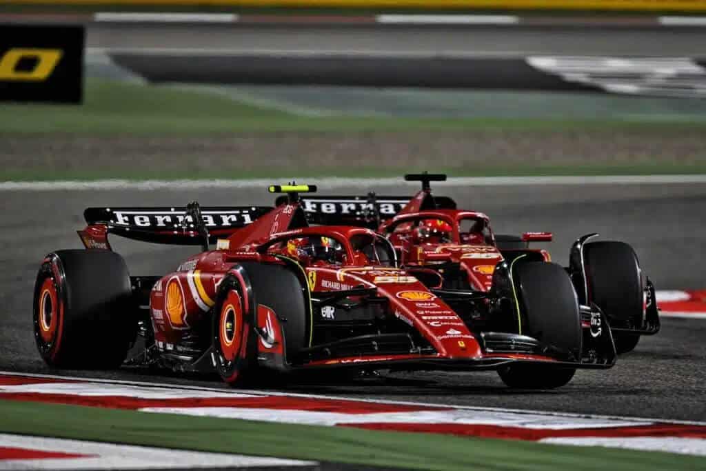 La imagen muestra a Carlos Sainz y Charles Leclerc, ambos pilotos de Fórmula 1 del equipo Ferrari, conduciendo sus coches en una pista de carreras. Los coches están adornados con el logotipo de Ferrari y varios patrocinadores, incluyendo Shell y Richard Mille. La escena parece ser de una carrera nocturna, indicada por la iluminación artificial y el entorno oscuro. Esta imagen es interesante y relevante porque captura un momento de competencia entre dos compañeros de equipo, Sainz y Leclerc, quienes son pilotos destacados para el equipo Ferrari en la Fórmula 1.