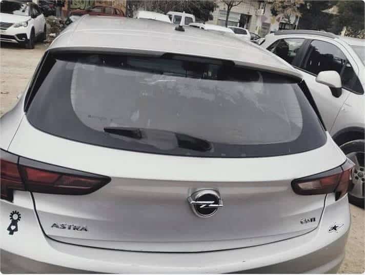 La imagen muestra la vista trasera de un coche Opel Astra blanco estacionado en un aparcamiento junto a otros vehículos. El coche tiene el logotipo de Opel en el centro del maletero, el nombre del modelo "ASTRA" en el lado izquierdo y el nivel de equipamiento "GSM" en el lado derecho. Hay dos pegatinas en el coche: una cerca de la luz trasera izquierda y otra en la esquina inferior derecha del maletero. Esta imagen es ficticia y se utiliza para un estudio que demuestra las habilidades de marketing de Miana.