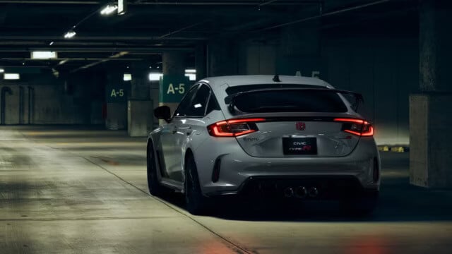 Vista trasera de un Honda Civic Type R 2025 en color gris plateado, estacionado en un garaje subterráneo oscuro. Las luces traseras LED rojas están encendidas y se destaca el alerón deportivo negro.