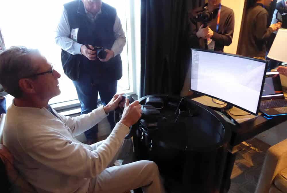 Hombre mayor probando un simulador de conducción con un volante y una pantalla, utilizado para evaluar tecnologías de seguridad y asistencia al conductor.