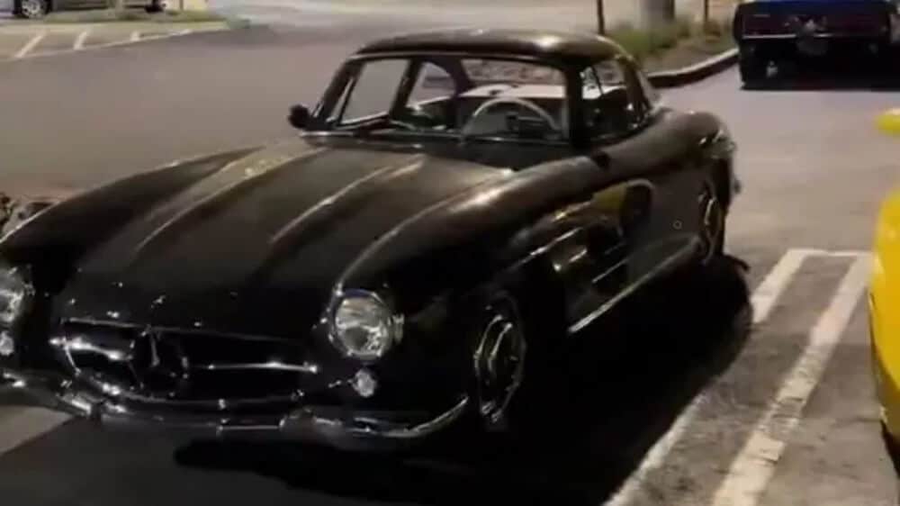 Un Mercedes-Benz 300SL Gullwing negro clásico está estacionado en un aparcamiento. Este coche es notable por sus distintivas puertas de ala de gaviota y es considerado un automóvil vintage icónico y de gran valor. No hay problemas matemáticos ni de tareas en la imagen.