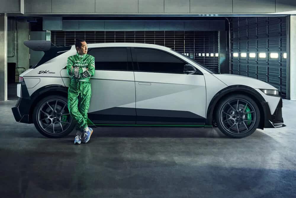 Keiichi Tsuchiya, apoyado en el lateral del Hyundai Ioniq 5 N DK Edition, en un garaje, con el coche en perfil completo.