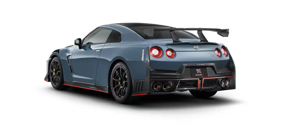 "Vista trasera de un Nissan GT-R R35 azul estacionado. Destacan sus luces traseras dobles redondas, el prominente alerón trasero y un difusor con cuatro salidas de escape cromadas. La insignia 'GT-R' resalta en el centro de la parte trasera. El vehículo está ubicado en un entorno al aire libre, subrayando su diseño deportivo y elegante en el contexto de su fin de producción.