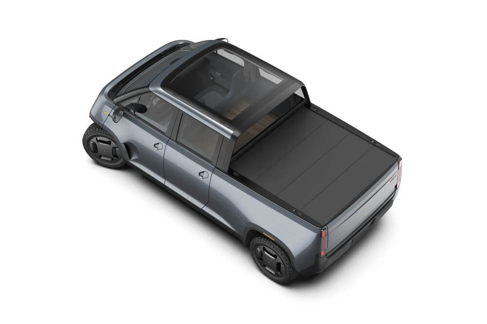 "Vista elevada y trasera de una camioneta eléctrica azul de la marca 'Telo Trucks'. La camioneta muestra un diseño moderno con líneas aerodinámicas, un techo de vidrio que deja ver el interior, y una caja de carga cubierta con una tapa rígida. Las llantas tienen un diseño distintivo que complementa el estilo innovador del vehículo.