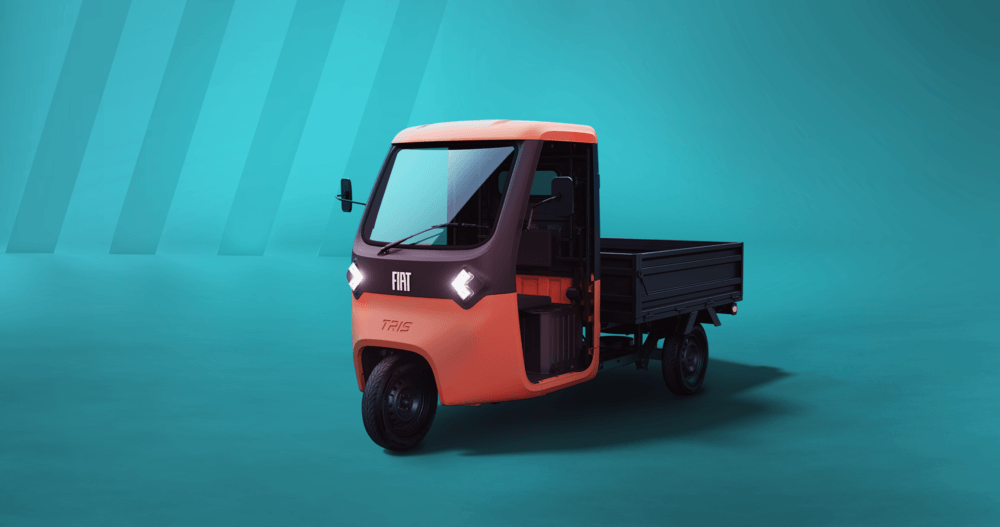 La imagen muestra un isocarro FIAT clásico, un pequeño vehículo de tres ruedas con un diseño compacto y encantador. Su carrocería es de color rojo vibrante con detalles cromados, lo que le da un aire retro y nostálgico. La cabina es cerrada, y la parte trasera está diseñada para el transporte de carga o pasajeros. Se encuentra estacionado en un entorno urbano con arquitectura tradicional, resaltando su estilo vintage y su carácter pintoresco.