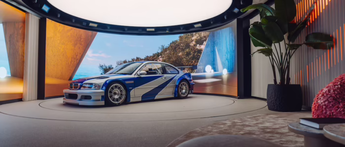 bmw-m3-gtr-nfs-hd-12 La imagen muestra la vista trasera de un BMW M3 GTR, un coche de carreras de alto rendimiento, estacionado en un garaje o taller con poca iluminación. El coche cuenta con un gran alerón trasero, lo que indica que está diseñado para carreras de alto rendimiento. La iluminación en el garaje resalta las características aerodinámicas del coche y su diseño elegante, haciéndolo visualmente impactante y relevante para los entusiastas del automovilismo o aquellos interesados en la ingeniería de coches de carreras. Este coche es famoso por su aparición en el videojuego 'Need for Speed: Most Wanted', donde juega un papel central.