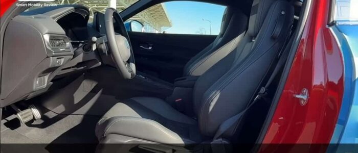 El interior de un Honda Prelude 2026, específicamente los asientos delanteros y el área del tablero. El coche parece ser un modelo deportivo o de lujo con una disposición de asientos 2+2, lo que significa que tiene dos asientos delanteros y dos asientos traseros más pequeños. El texto en la imagen está en japonés y dice: 'パッケージングは引き締まった2+2レイアウトに,' que se traduce como 'El embalaje es un diseño compacto de 2+2.' La imagen destaca el diseño y la disposición de los asientos del coche, lo cual puede ser de interés para posibles compradores o entusiastas del automovilismo.