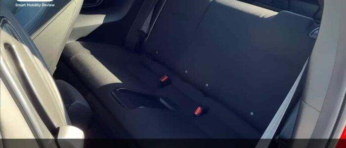 "El área del asiento trasero de un Honda Prelude 2026. Los asientos están tapizados en tela oscura y se pueden ver los broches de los cinturones de seguridad. El interior parece limpio y moderno. El texto superpuesto en la imagen está en japonés y dice: '走りと“デートカー”の快適性を高い次元で両立する,' que se traduce como 'Combinando el rendimiento de conducción y la comodidad de un "coche de citas" a un alto nivel.