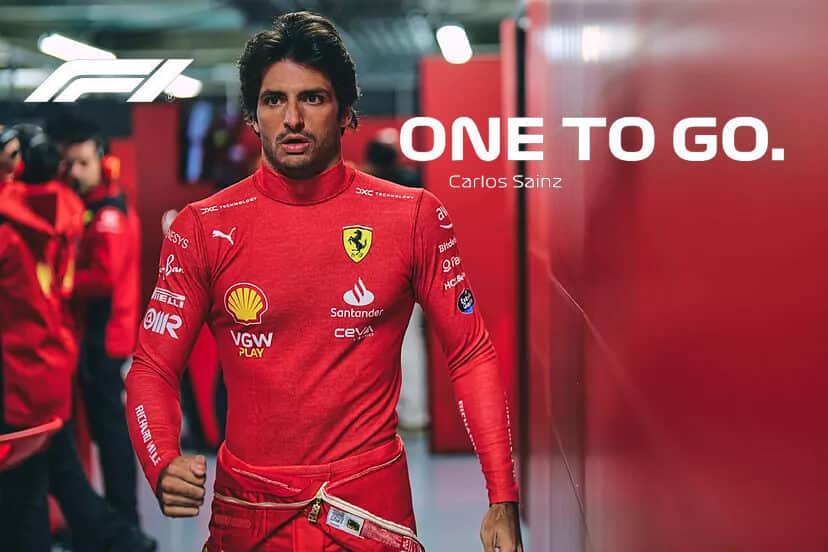 La imagen muestra a Carlos Sainz con su traje de carreras rojo de Ferrari, adornado con varios logotipos de patrocinadores como Puma, Santander y otros. Sainz está caminando en lo que parece ser el área de boxes o el pit lane. El texto en la imagen dice: "ONE TO GO. Carlos Sainz." También se puede ver el logotipo de la F1 en la esquina superior izquierda. Esta imagen es significativa porque representa la última carrera de Sainz con Ferrari, que tendrá lugar en el Gran Premio de Abu Dhabi