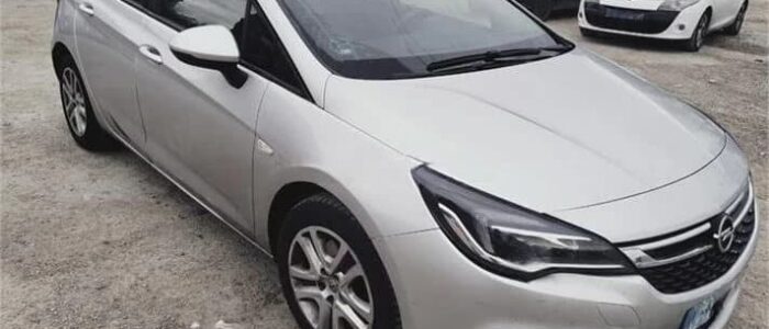 La imagen muestra un Opel Astra plateado estacionado en un aparcamiento junto a otros vehículos. El coche está orientado en un ángulo que destaca su diseño elegante, los faros delanteros y la parrilla con el logotipo de Opel. Esta imagen es ficticia y se utiliza para un estudio que demuestra las habilidades de marketing de Miana.