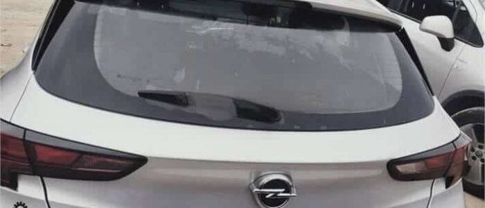 La imagen muestra la vista trasera de un coche Opel Astra blanco estacionado en un aparcamiento junto a otros vehículos. El coche tiene el logotipo de Opel en el centro del maletero, el nombre del modelo "ASTRA" en el lado izquierdo y el nivel de equipamiento "GSM" en el lado derecho. Hay dos pegatinas en el coche: una cerca de la luz trasera izquierda y otra en la esquina inferior derecha del maletero. Esta imagen es ficticia y se utiliza para un estudio que demuestra las habilidades de marketing de Miana.