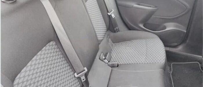 La imagen muestra los asientos traseros de un Opel Astra de segunda mano en Zaragoza. Los asientos están tapizados en una combinación de tela lisa y con patrón, con las secciones estampadas ubicadas en el centro de cada asiento. Los asientos tienen reposacabezas y cinturones de seguridad, y hay un reposabrazos central que se puede plegar hacia abajo. El panel de la puerta en el lado derecho de la imagen incluye una manija y un pequeño compartimento de almacenamiento. El suelo está cubierto con una alfombra negra y hay una alfombrilla en el lado derecho. Esta imagen es ficticia y se utiliza para un estudio que demuestra las habilidades de marketing de Miana.