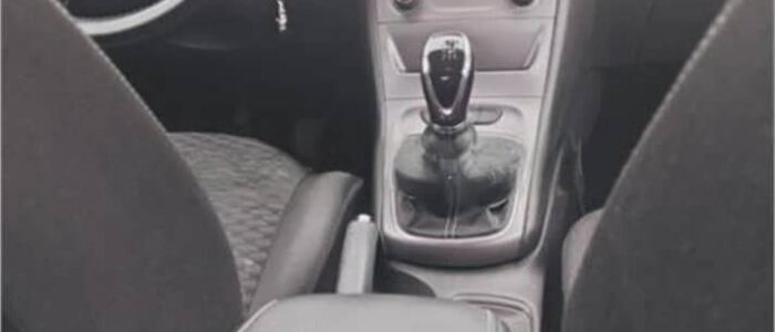 La imagen muestra la consola central de un Opel Astra de segunda mano en Zaragoza. Se puede ver la palanca de cambios, que parece ser de transmisión manual, junto con la palanca del freno de mano. También se observan los controles del sistema de climatización, incluyendo perillas y botones. El volante y parte del asiento del conductor también son visibles. Esta imagen es ficticia y se utiliza para un estudio que demuestra las habilidades de marketing de Miana.