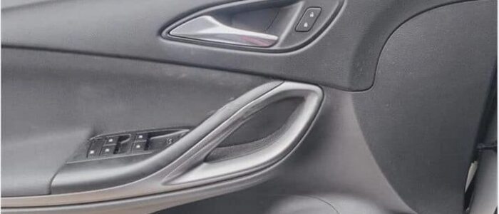 La imagen muestra el panel interior de la puerta de un Opel Astra de segunda mano en Zaragoza. El panel incluye una manija de puerta metálica, un conjunto de botones de control de ventanas y un botón de ajuste del espejo lateral. Los botones de control de ventanas están ubicados en un panel negro cerca del reposabrazos. El botón de ajuste del espejo lateral está situado cerca de la parte superior del panel de la puerta. Esta imagen es ficticia y se utiliza para un estudio que demuestra las habilidades de marketing de Miana.